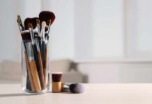 A collection of makeup brushes in a glass container on a table