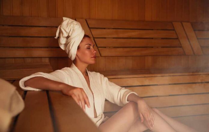 shutterstock_2449834593.jpg Woman relaxing in a sauna wearing a robe and towel