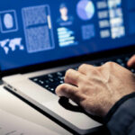 Close-up of hands typing on a laptop with data visualizations on the screen