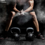 Athlete preparing to lift kettlebells in a gym with chalk dust in the air