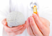 A medical professional holding a brain model in one hand and a yellow supplement capsule in the other
