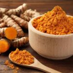 Turmeric powder in a wooden bowl with fresh turmeric roots