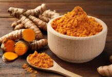 Supplement Aisle Lies About Turmeric Turmeric powder in a wooden bowl with fresh turmeric roots