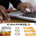 Person using a calorie counter app on a tablet while working on a laptop