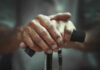 Close-up of elderly hands resting on a walking cane