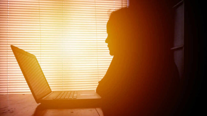 shutterstock1752543413jpg Silhouette of a person working on a laptop with sunlight streaming through blinds