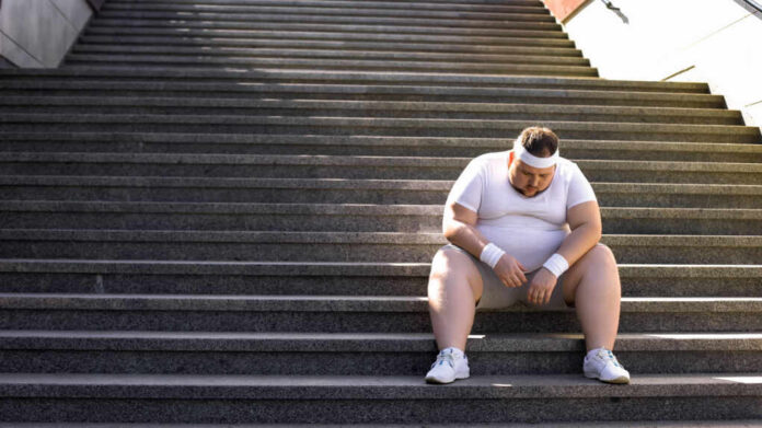 An exhausted man in sportswear sitting on outdoor stairs, looking down.