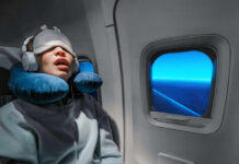 A passenger sleeping on an airplane with headphones and an eye mask