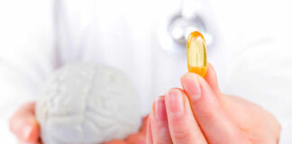 A medical professional holding a brain model in one hand and a yellow supplement capsule in the other