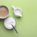 A cup of coffee, a bowl of sugar, and a creamer on a green background