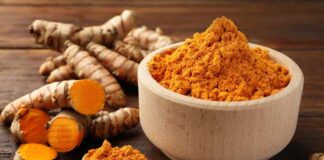 Turmeric powder in a wooden bowl with fresh turmeric roots