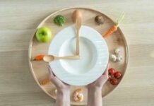 Hands holding a white plate surrounded by fresh vegetables and an egg