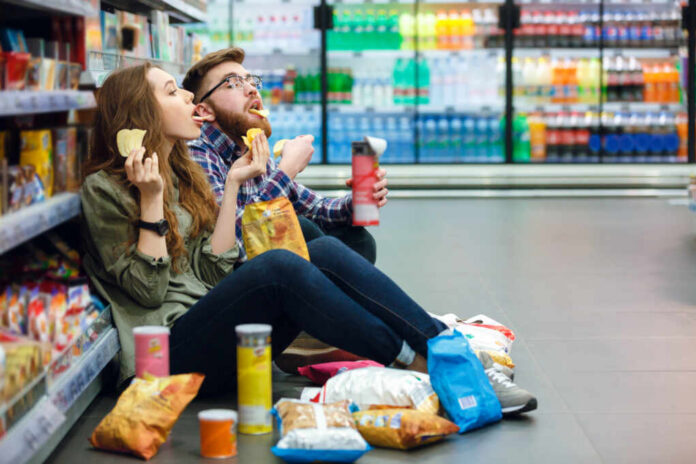 A young couple sitting on the floor of a grocery store enjoying snacks