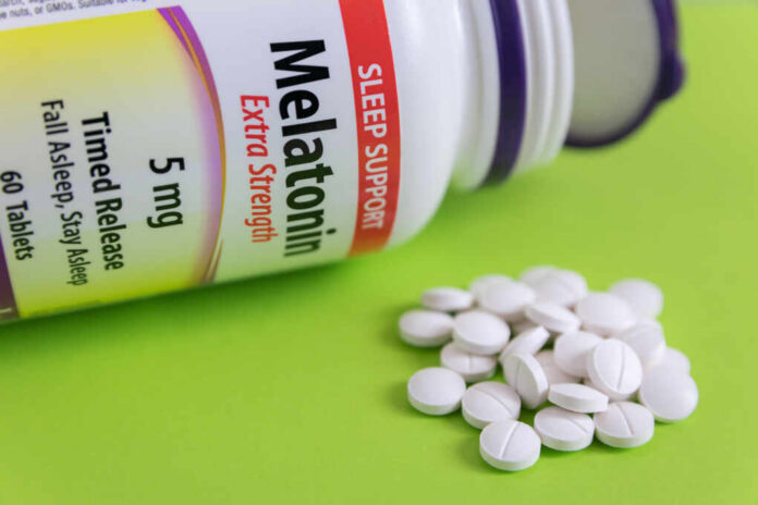 Bottle of melatonin tablets with some pills spilled on a green surface