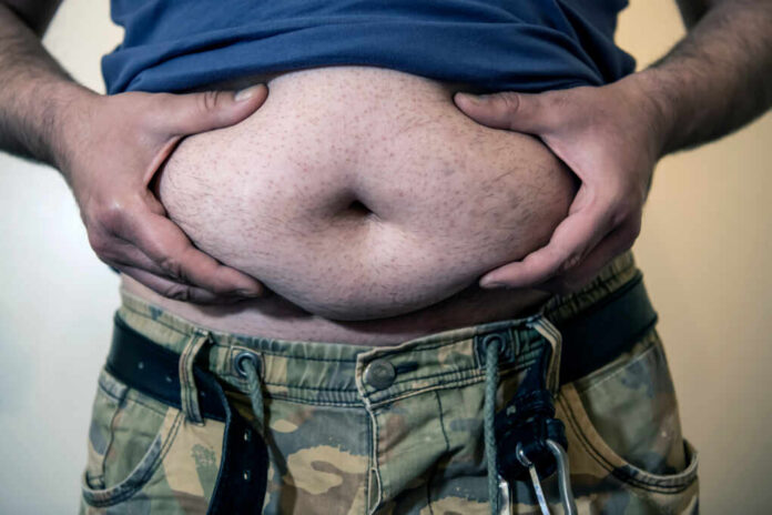 Mature,Man,In,Military,Pants,With,Big,Belly,Is,Having Man holding his belly with both hands, wearing a blue shirt and camouflage pants