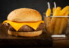 Close-up of a cheeseburger with a sesame seed bun and fries in the background