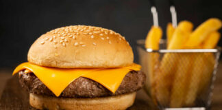 Close-up of a cheeseburger with a sesame seed bun and fries in the background