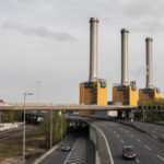 Industrial power plant with three tall smokestacks beside a highway