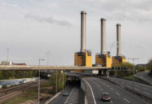 Coal Dust Cancer Crisis Industrial power plant with three tall smokestacks beside a highway