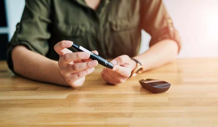 Diabetes,,Finger,And,Monitor,With,Person,At,Table,In,Home Person using a blood glucose meter and a pen device for diabetes management