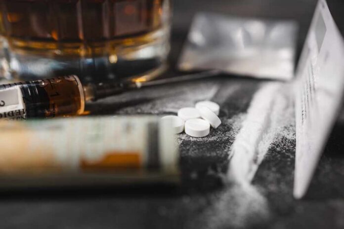 A close-up of a syringe, pills, and a glass of alcohol on a dark surface