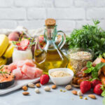 A variety of fresh foods including fruits, vegetables, and oils arranged on a table