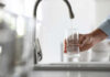 A hand holding a glass under a kitchen faucet while water is being poured into it