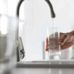 A hand holding a glass under a kitchen faucet while water is being poured into it