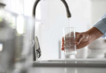 Tap Water Chemical Linked To Dementia A hand holding a glass under a kitchen faucet while water is being poured into it