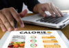 Protein Timing Mistake Sabotaging Your Diet Person using a calorie counter app on a tablet while working on a laptop