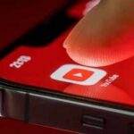 Finger tapping YouTube app icon on smartphone screen