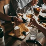 Hands toasting wine glasses over a cheese board