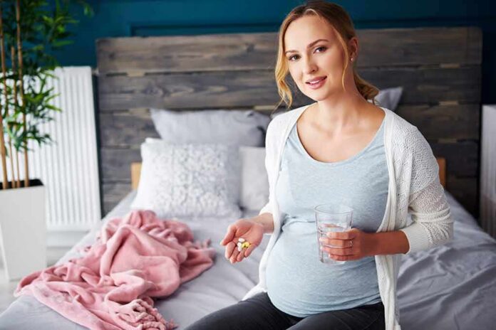Pregnant woman sitting on bed holding pills and a glass of water
