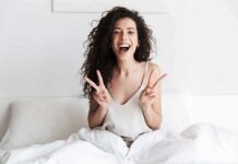 New Metrics Upend Happiness Obsession Smiling woman on bed showing double peace signs