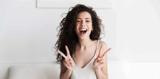 Smiling woman on bed showing double peace signs