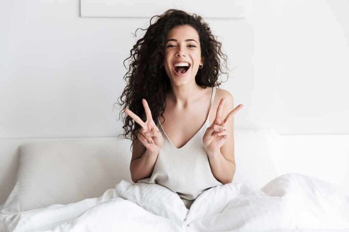 shutterstock_1115846087 Smiling woman on bed showing double peace signs