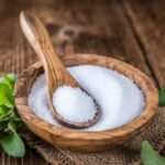 Wooden bowl of white granules with spoon and green leaves