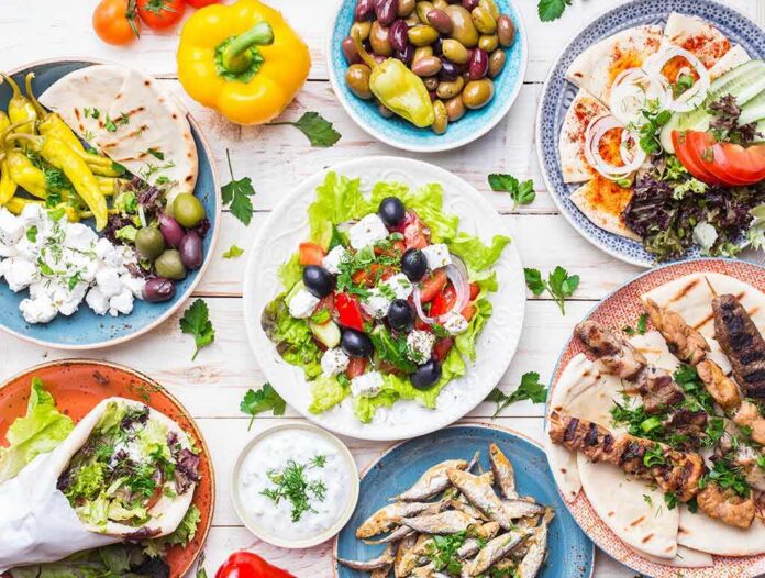 shutterstock_646209787 Greek meze spread with salad, olives, pita, and grilled skewers