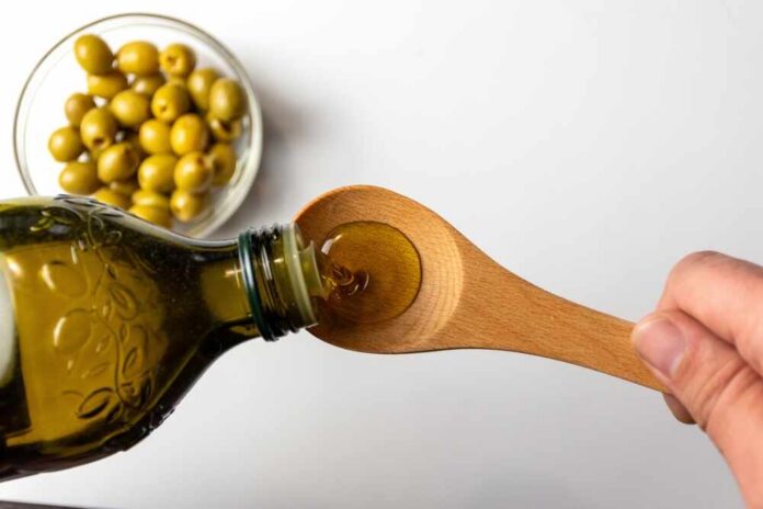 Pouring olive oil from a bottle into a wooden spoon