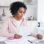 Woman reviewing bills at a kitchen table with a laptop