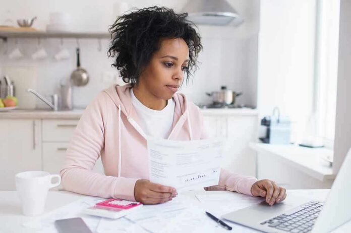 1783890279381-6oy2yr-shutterstock-1100063891 Woman reviewing bills at a kitchen table with a laptop
