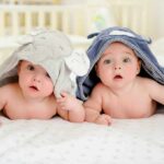 two babies under hooded towels on a bed