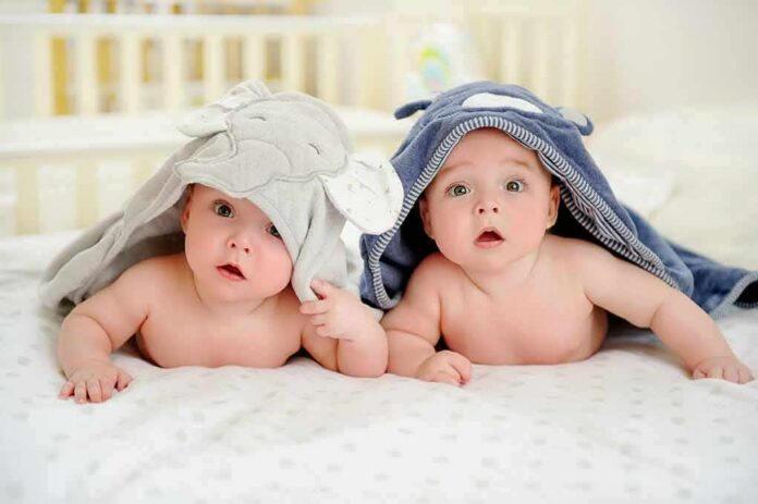 two babies under hooded towels on a bed