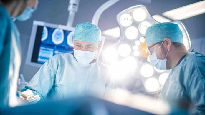 shutterstock_1152711494 Surgeons in operating room under bright surgical lights