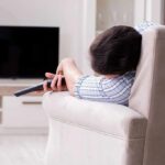 Person lying on a sofa holding a TV remote