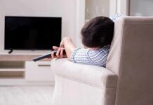 Person lying on a sofa holding a TV remote