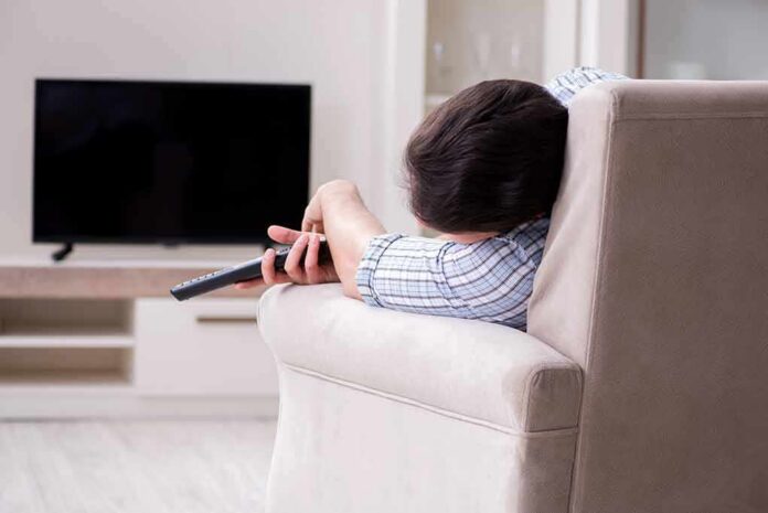 Person lying on a sofa holding a TV remote