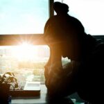 silhouetted person at a desk with head in hands
