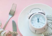 This Eating Pattern Was Linked To Better Memory In Seniors Pink alarm clock on a white plate with fork, knife, and measuring tape
