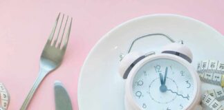 Pink alarm clock on a white plate with fork, knife, and measuring tape